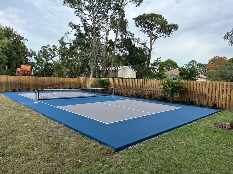 After: New backyard pickleball court with blue and gray surface, net and privacy fence