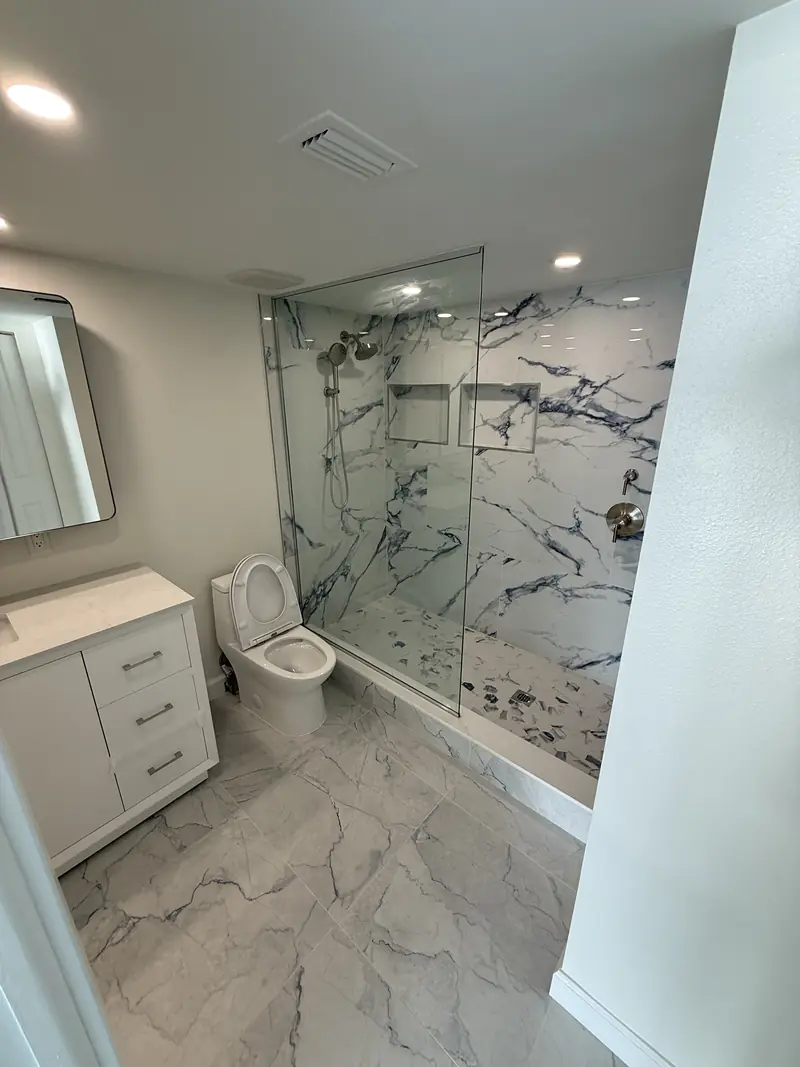 Bathroom remodel with marble-look porcelain shower and floor, glass panel and white vanity in Sarasota, FL