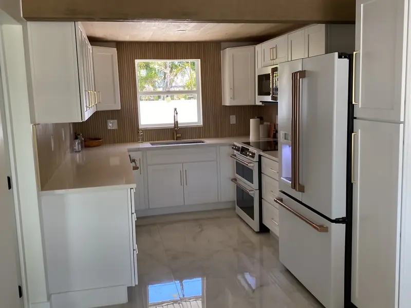 Bright white kitchen with quartz counters, white appliances with copper handles and polished tile floor in Holmes Beach, FL