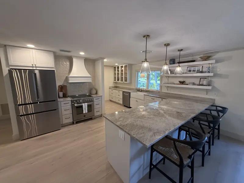 Remodeled kitchen with white shaker cabinets, quartzite island seating four, range hood and open shelving in Sarasota, FL