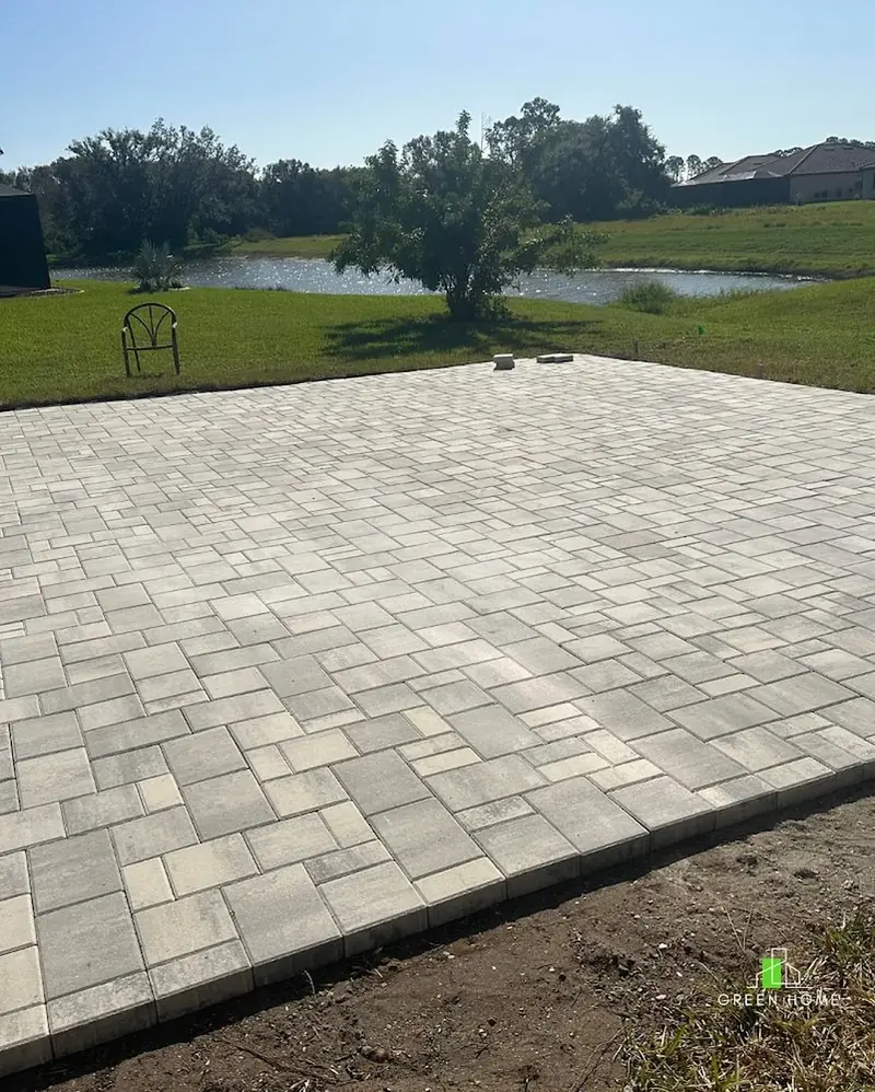 New gray paver patio installed in a backyard overlooking a pond