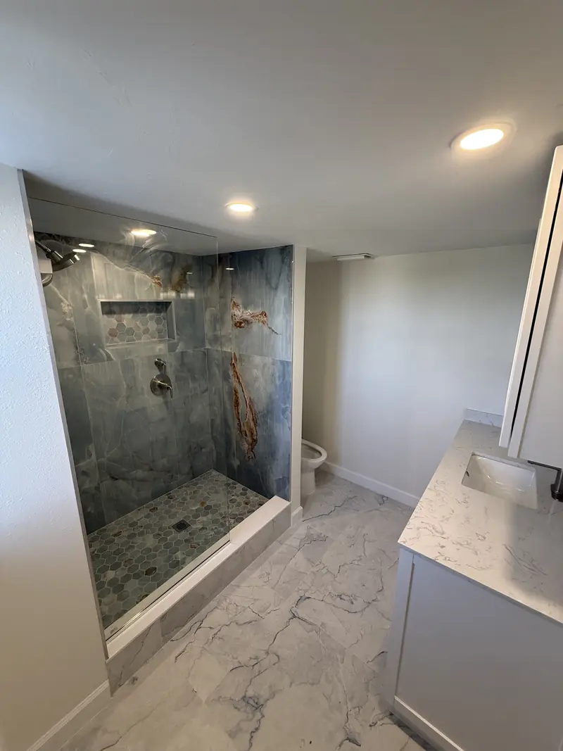 Remodeled walk-in shower with stone-look wall tile, pebble shower floor and marble-look porcelain floor in Sarasota, FL