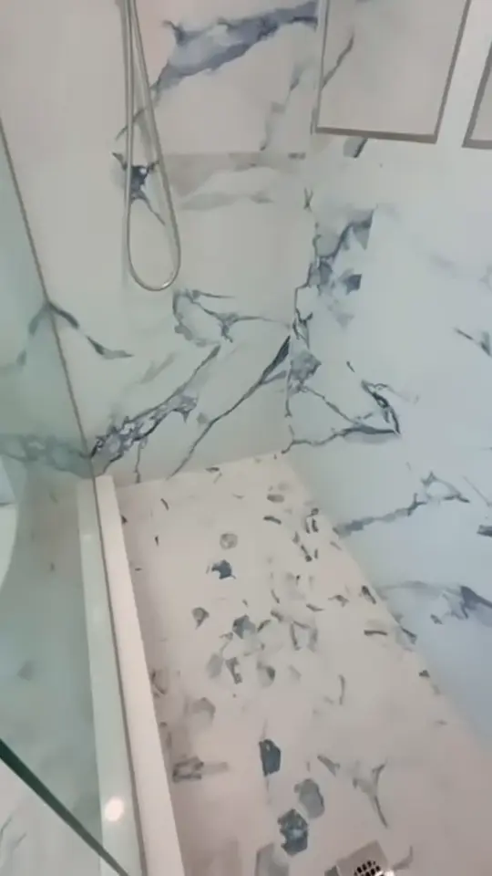 Walk-in shower remodel: An old tiled shower replaced with marble-look wall panels, two built-in niches and a pebble mosaic floor.